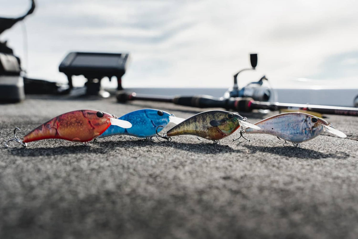 Three crankbait lures with treble hooks lying on a rough dock surface
