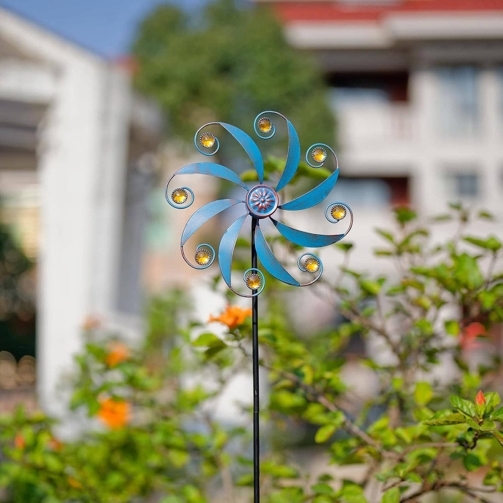 Blue metal wind spinner with curled blades and jeweled center, gold accent discs on black pole.