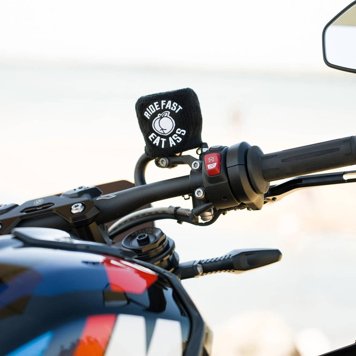 Black brake fluid reservoir cover sock with “RIDE FAST EAT ASS” logo on black handlebars