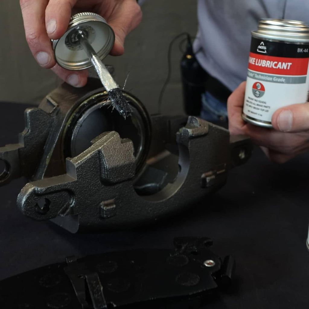 Technician applies silicone brake grease with brush-top, holding the can