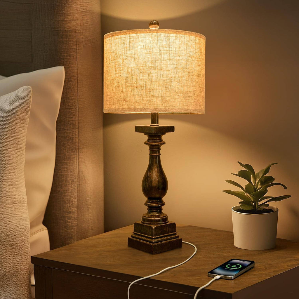 Table lamp with beige drum shade and dark turned base, phone charging on nightstand