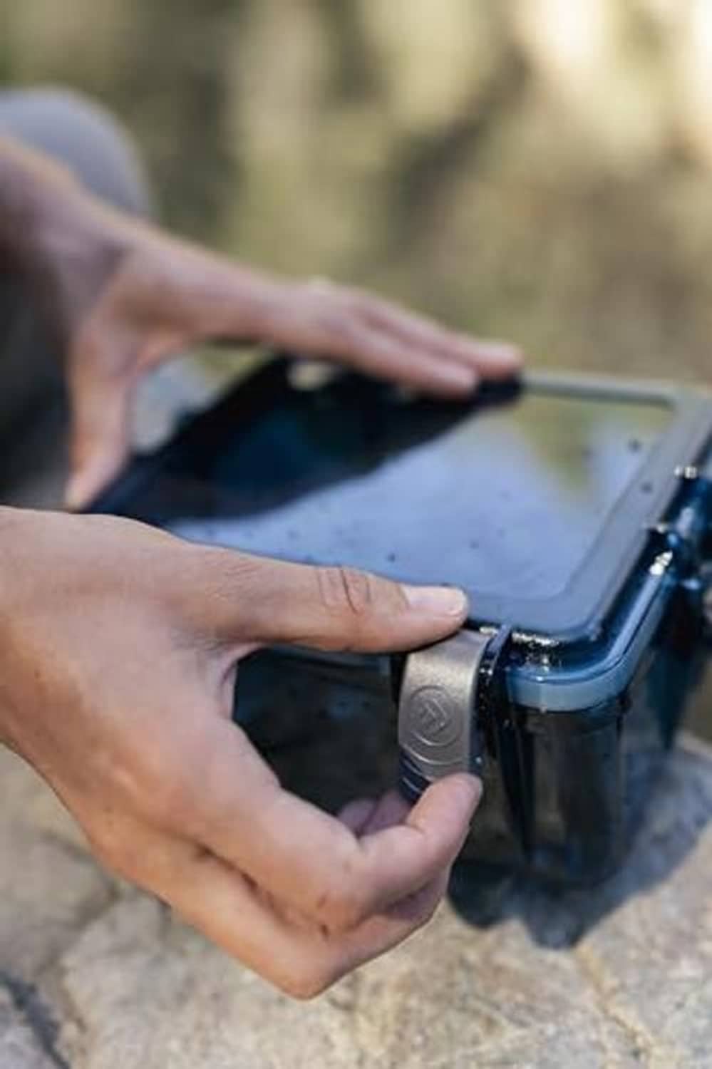 Hands unlatching a blue watertight box, clear lid and side latch locks