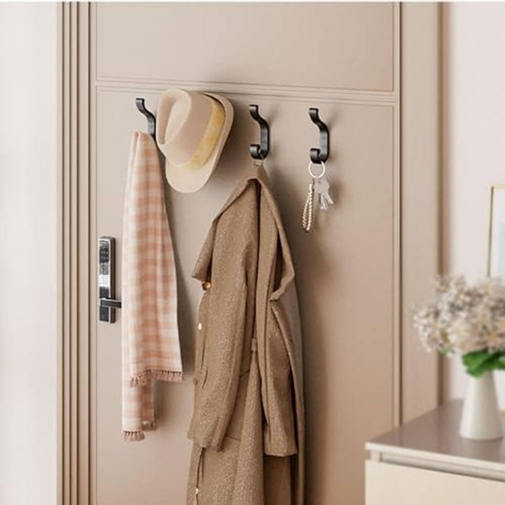 Four black coat hooks mounted on wall, holding coats and a tote bag