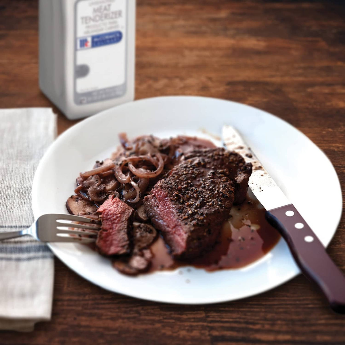 Plate of seasoned meat with tenderizer bottle partially visible on a tabletop