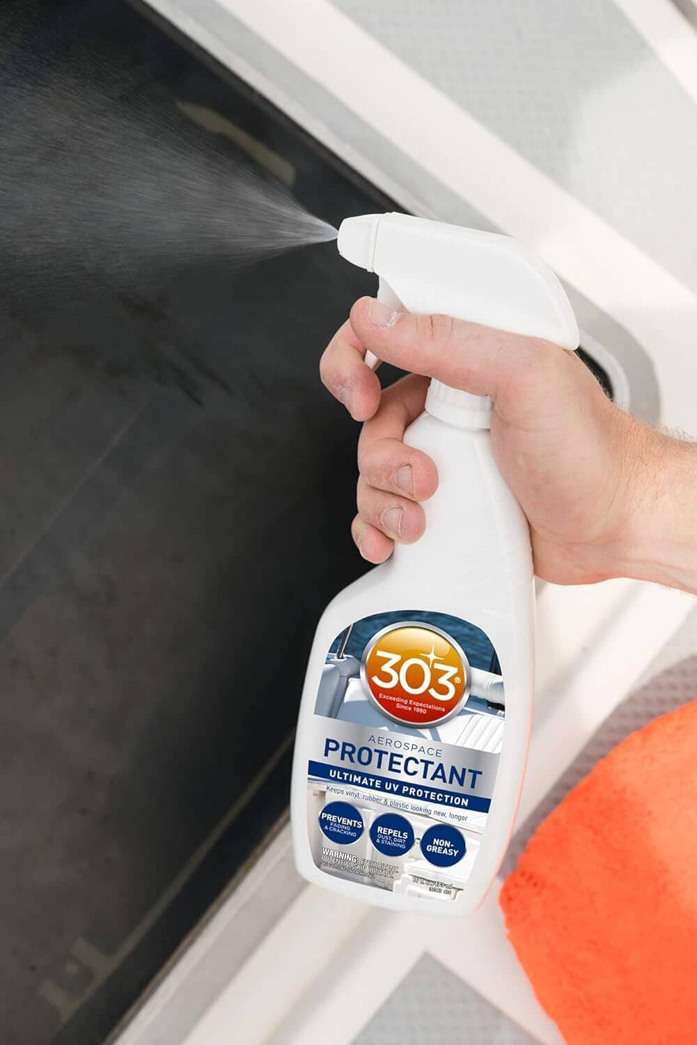 Hand spraying UV protectant from white trigger bottle onto a vinyl surface