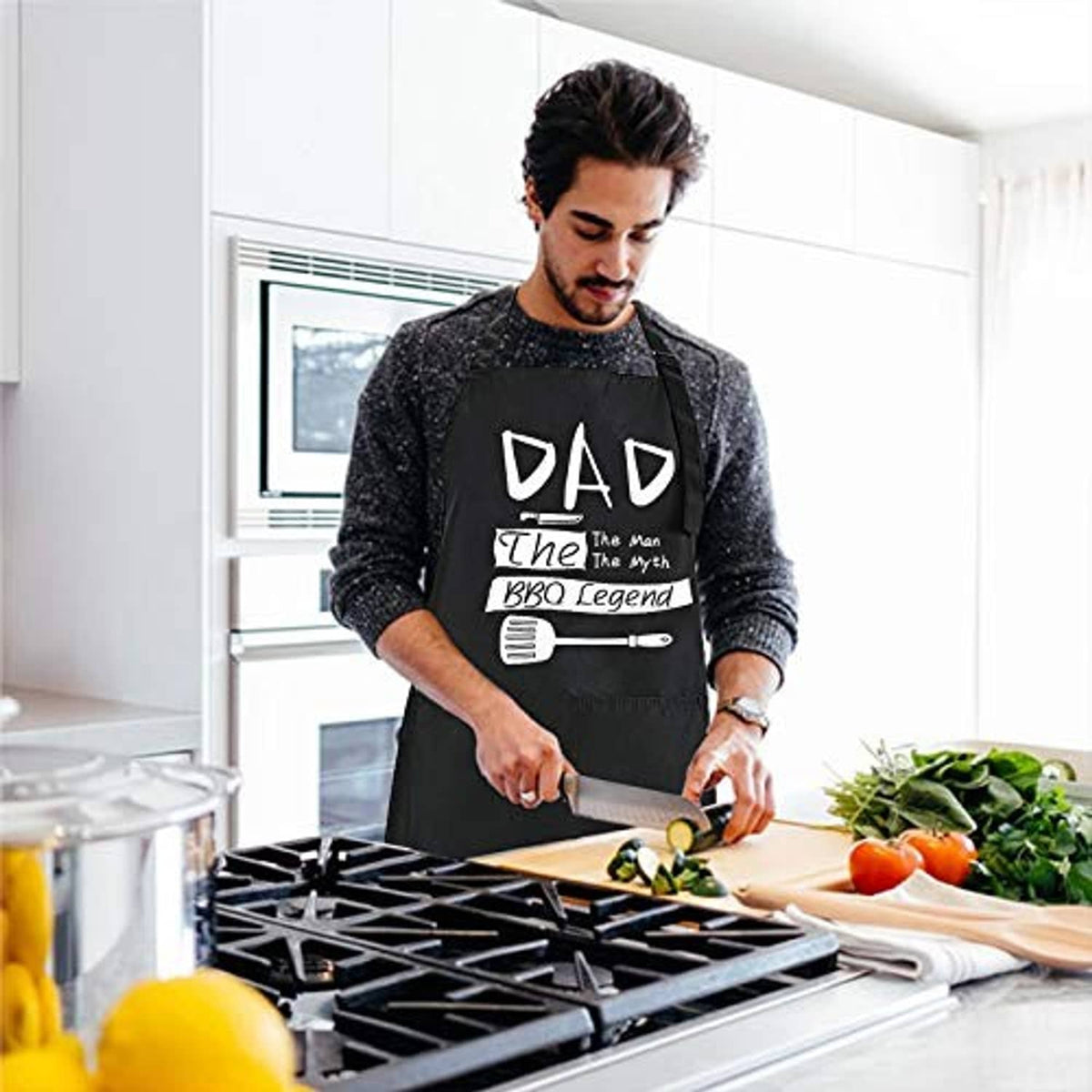 Man wearing black 'DAD The Man The Myth BBQ Legend' apron while cooking