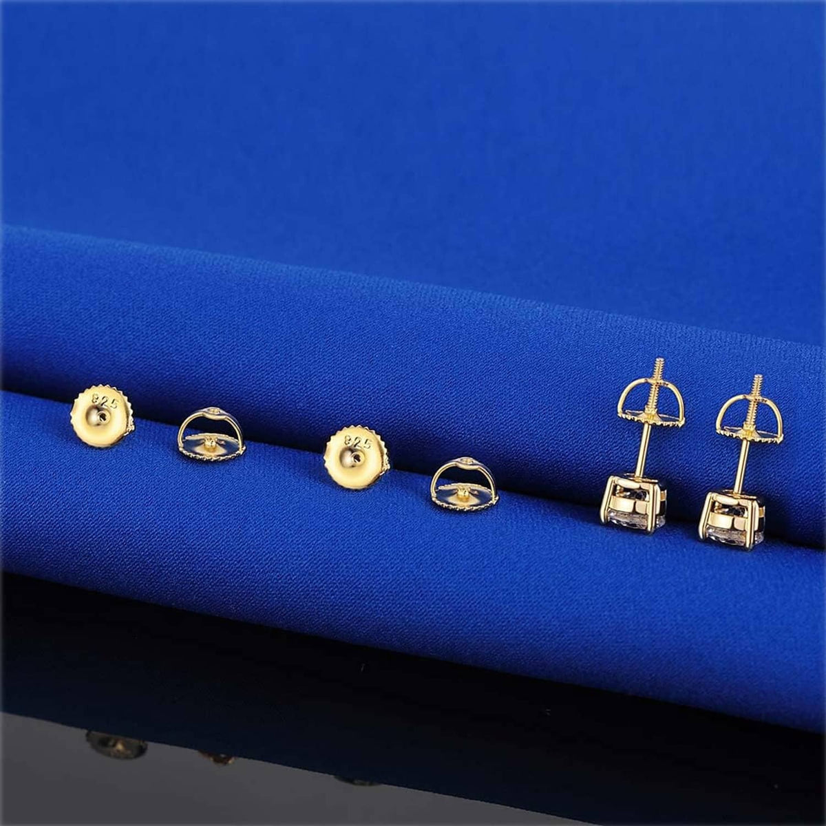 Gold-tone screw earring backs and posts displayed on blue fabric surface