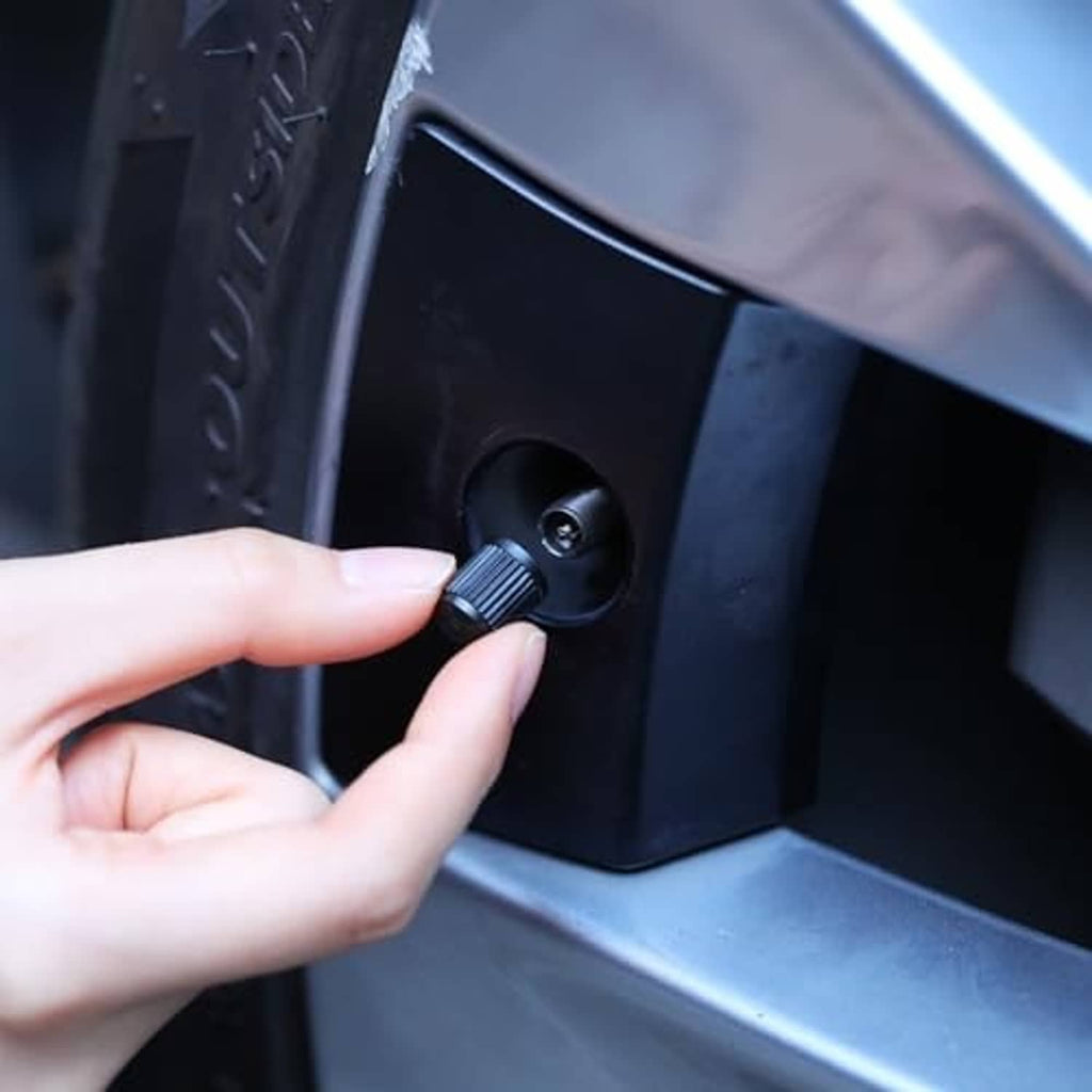 Hand installing a black plastic tire valve stem cap on a car wheel valve
