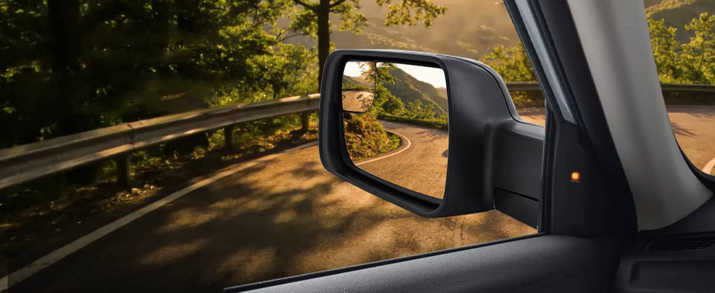Left driver-side mirror mounted on the door, reflecting a road