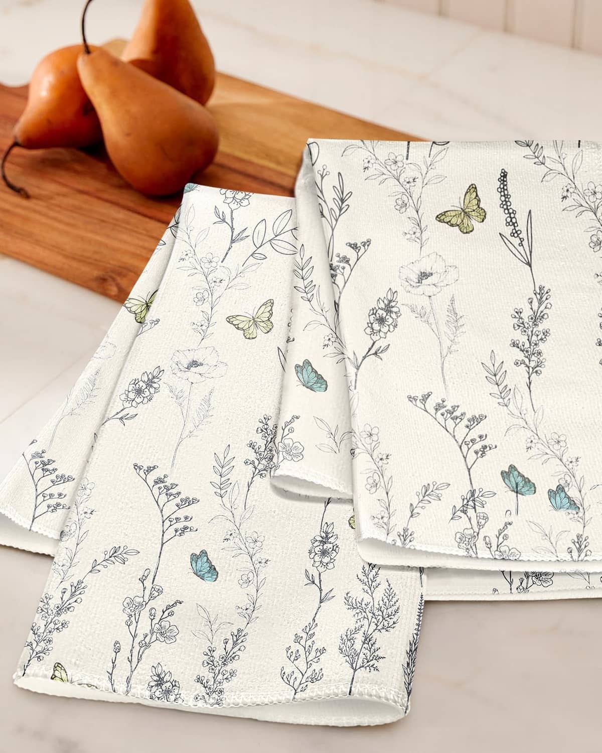 White kitchen towels set of 2 with botanical sprigs and butterfly motifs, folded on table