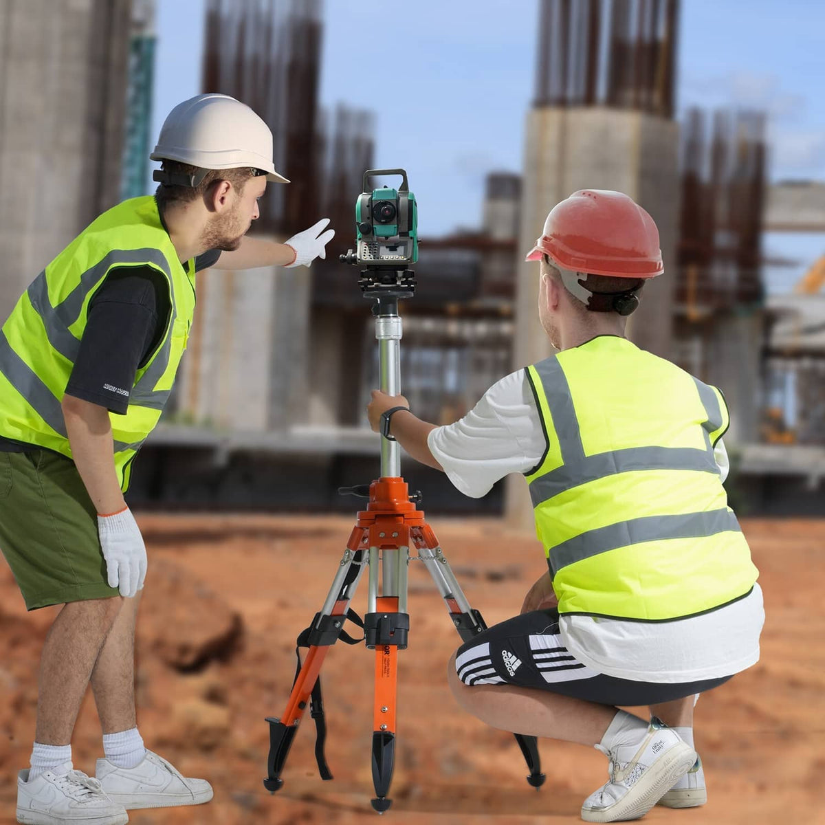 Orange laser level tripod stand set on site as workers operate the mounted level