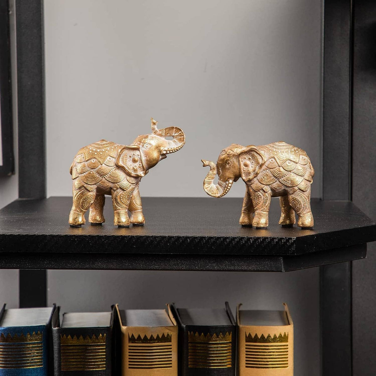 Gold elephant figurine pair on a black shelf, raised trunks, ornate details.
