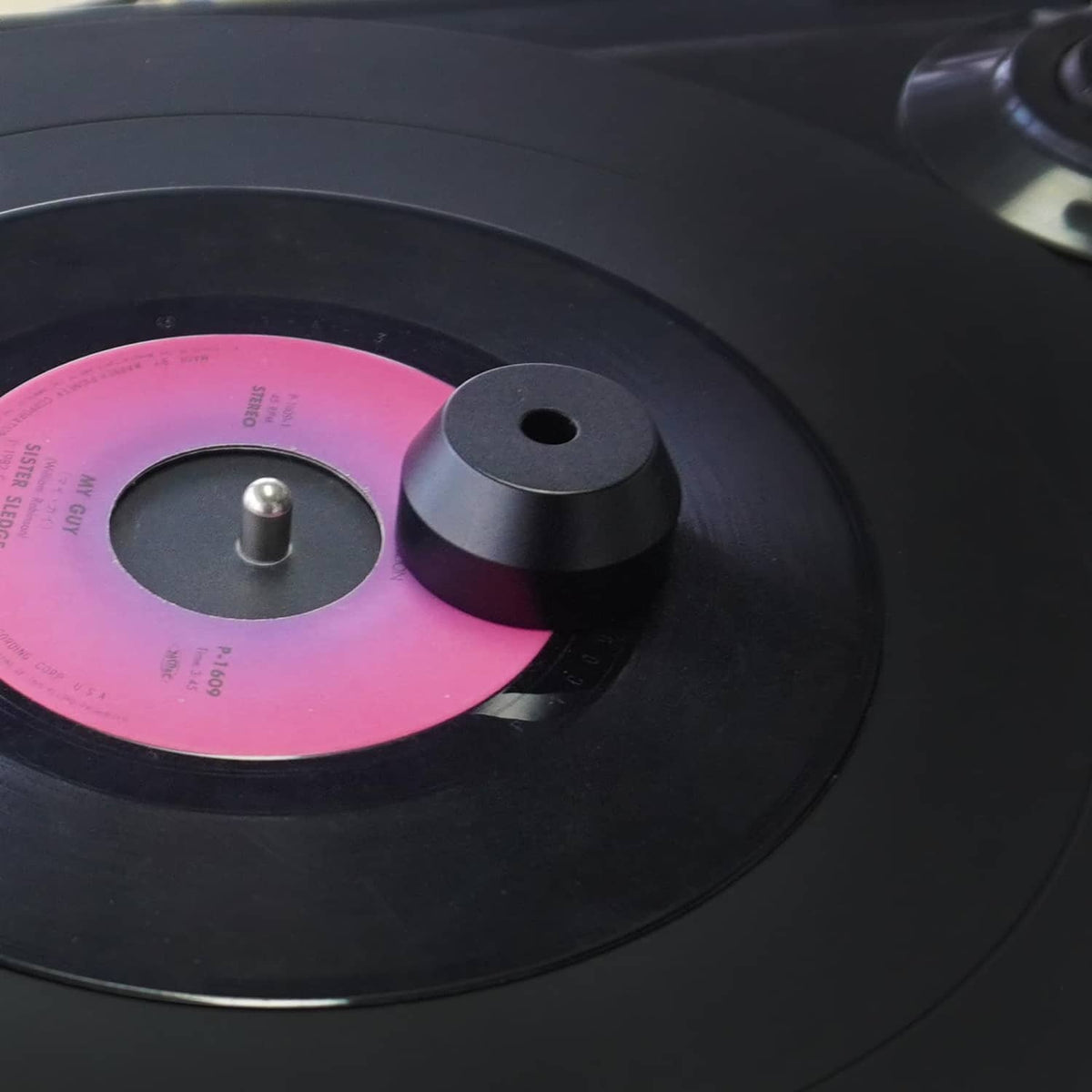 Black 45 RPM center adapter on a vinyl record with metal spindle post
