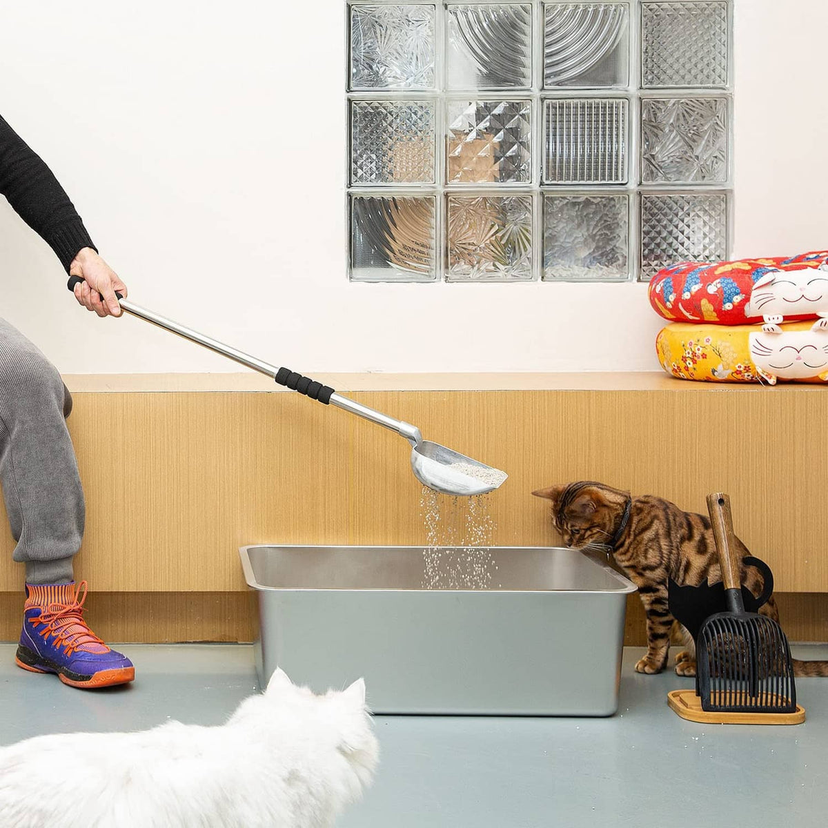 Long-handled metal cat litter scoop with black grip stirring litter in a box