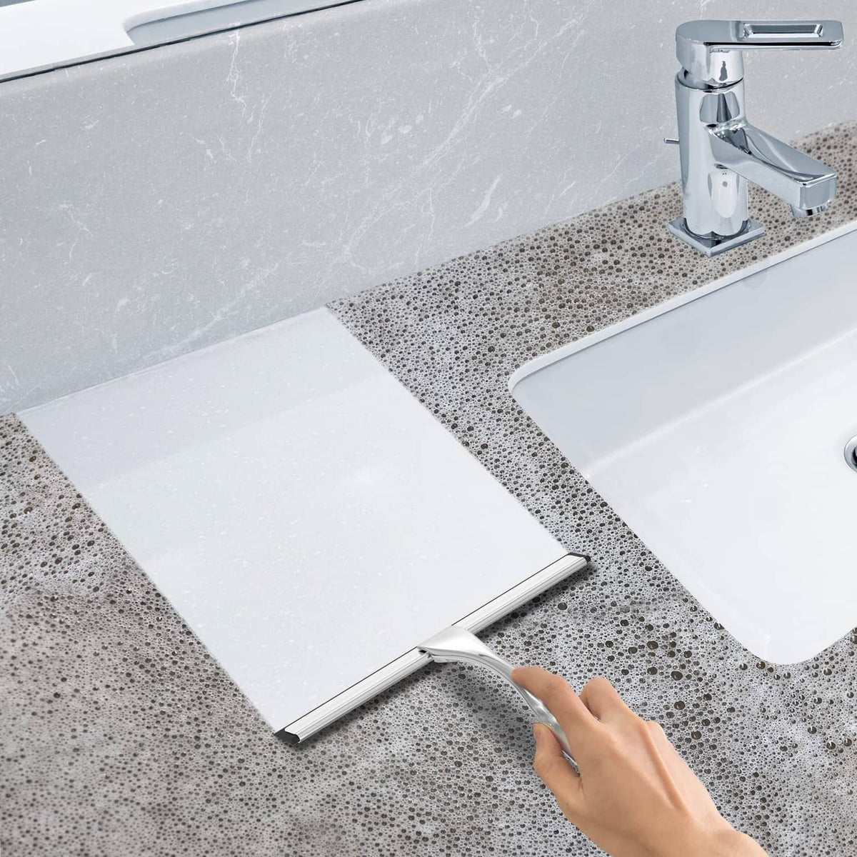 Stainless steel shower squeegee used to wipe water off a sink and counter area.