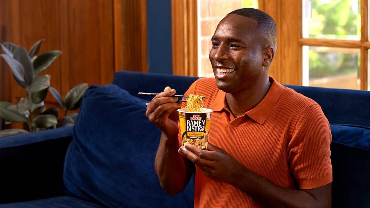 Person holding an instant ramen cup, orange polo, Ramen Bistro branding visible