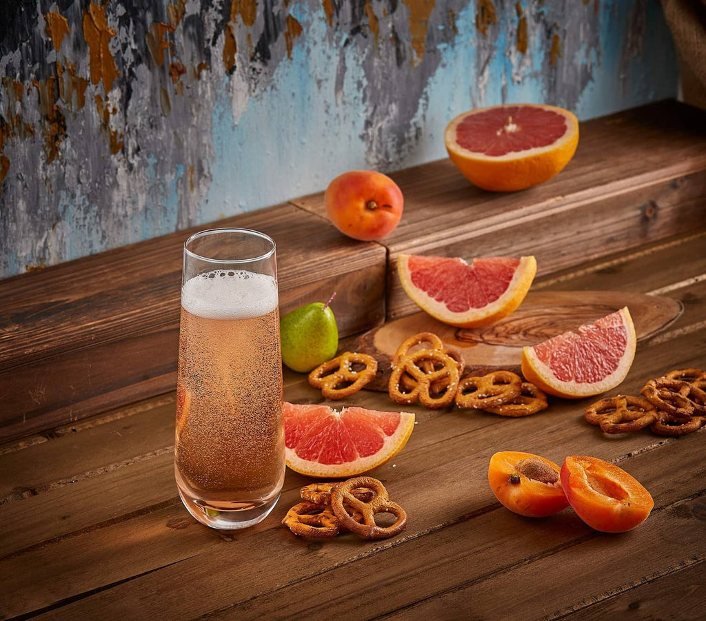 Stemless champagne flute with golden sparkling drink beside grapefruit slices and pretzels