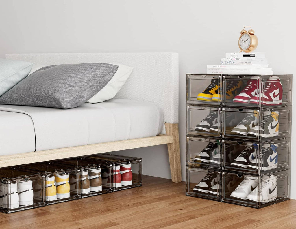 Clear stackable shoe storage boxes with sneakers visible through front doors near a bed