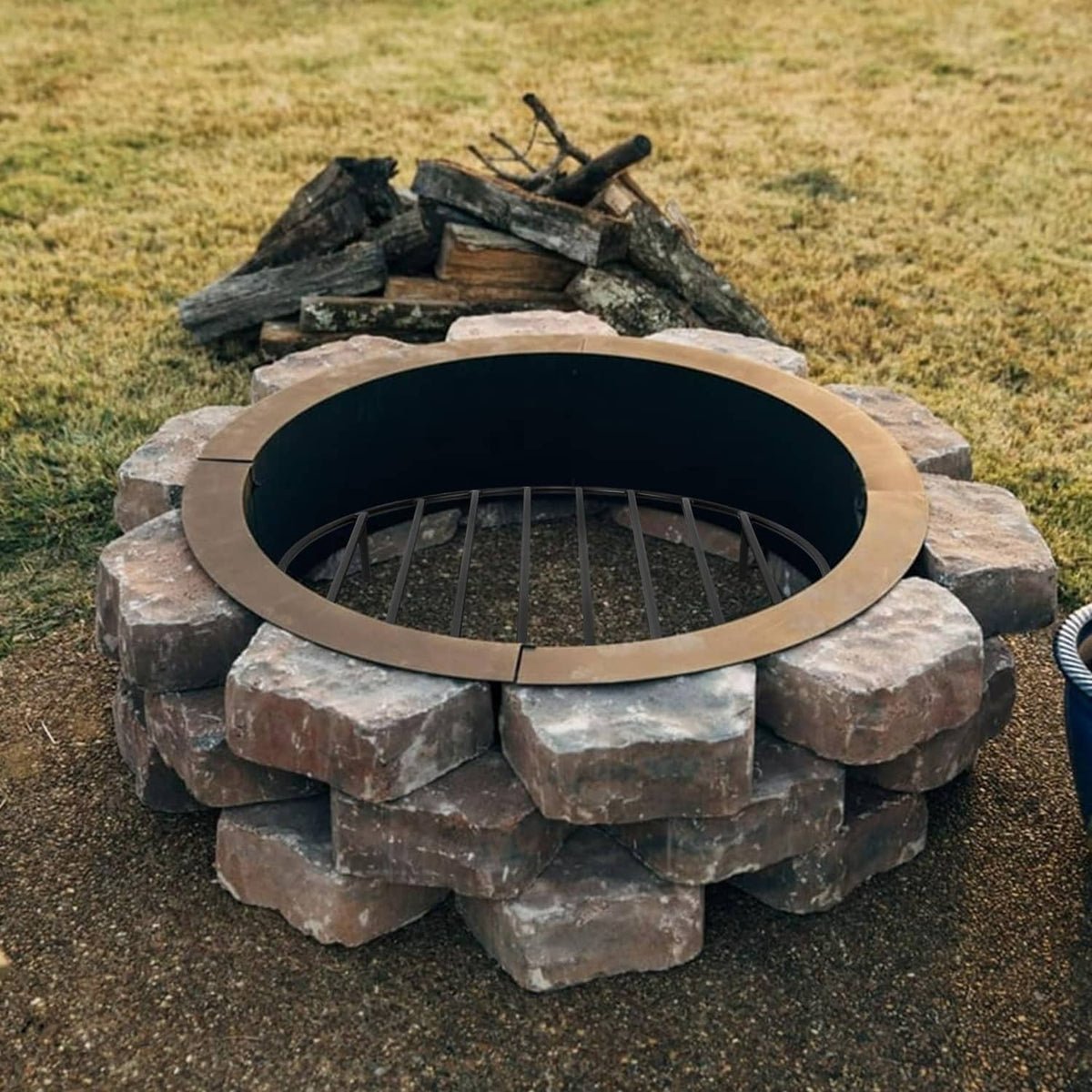 Black round fire pit grate resting inside a stone fire ring opening