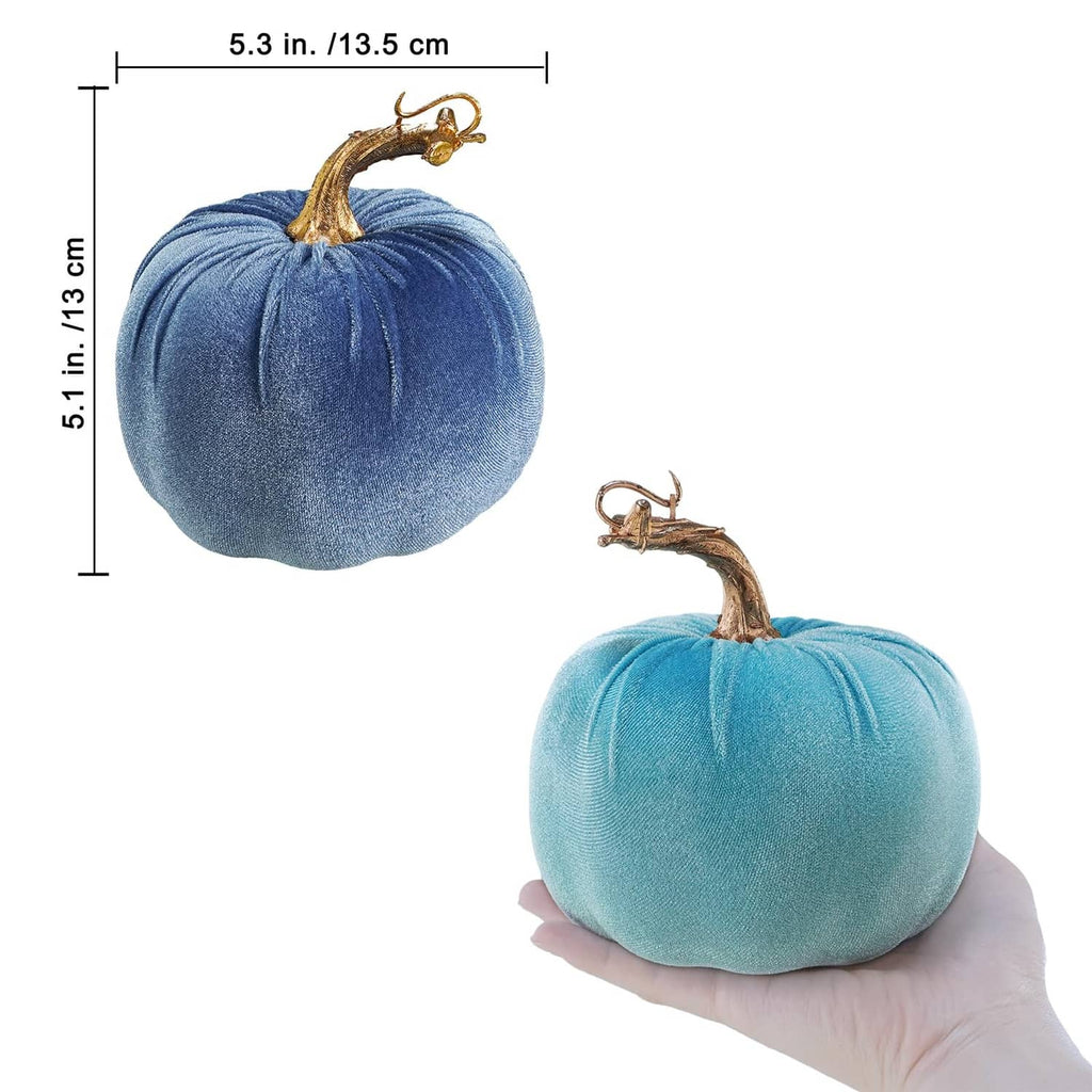 Two blue faux velvet pumpkins with gold curved stems and hanging loops, one held