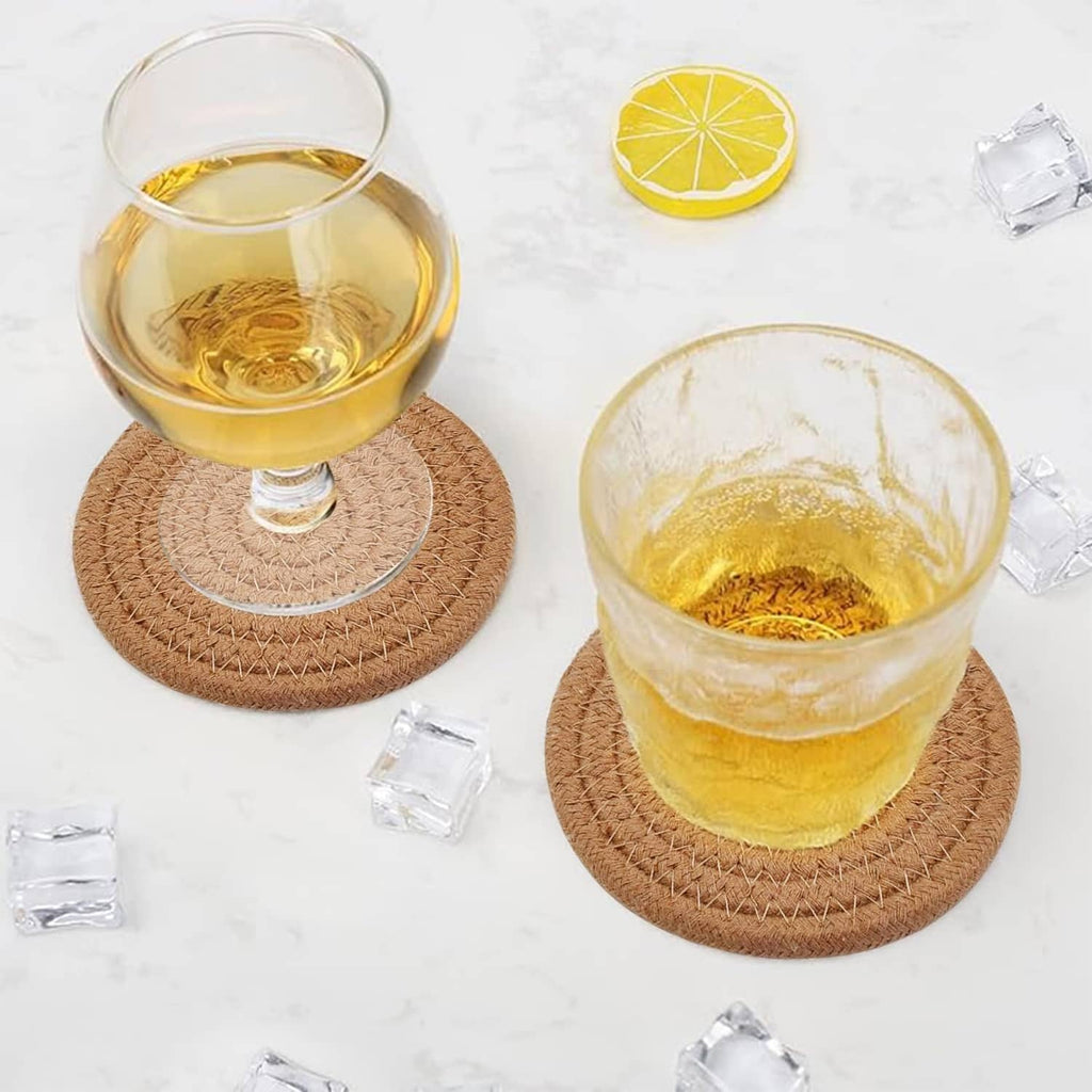 Two tan woven round coasters under drinks, clear glasses with yellow beverage and lemon