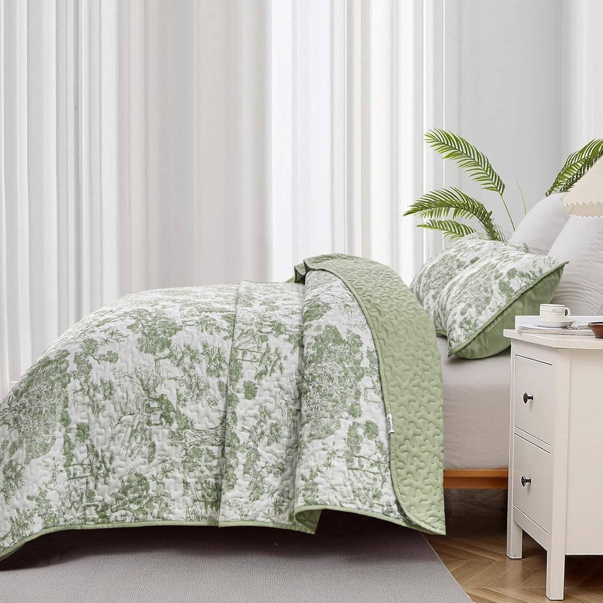 Sage green botanical quilt with matching pillow shams on a bed near a nightstand