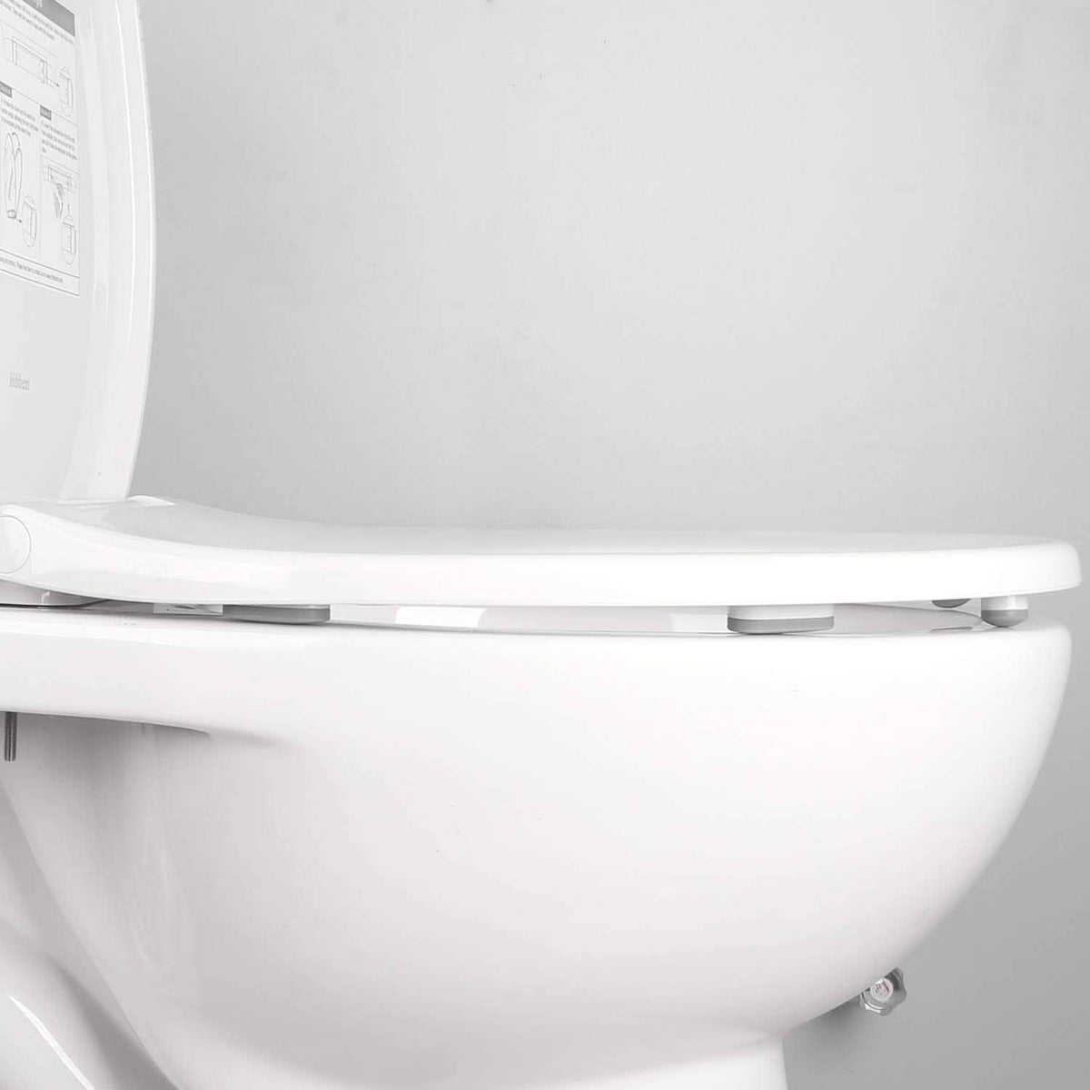 Close-up of gray toilet seat bumper pads under the lid on a white toilet seat