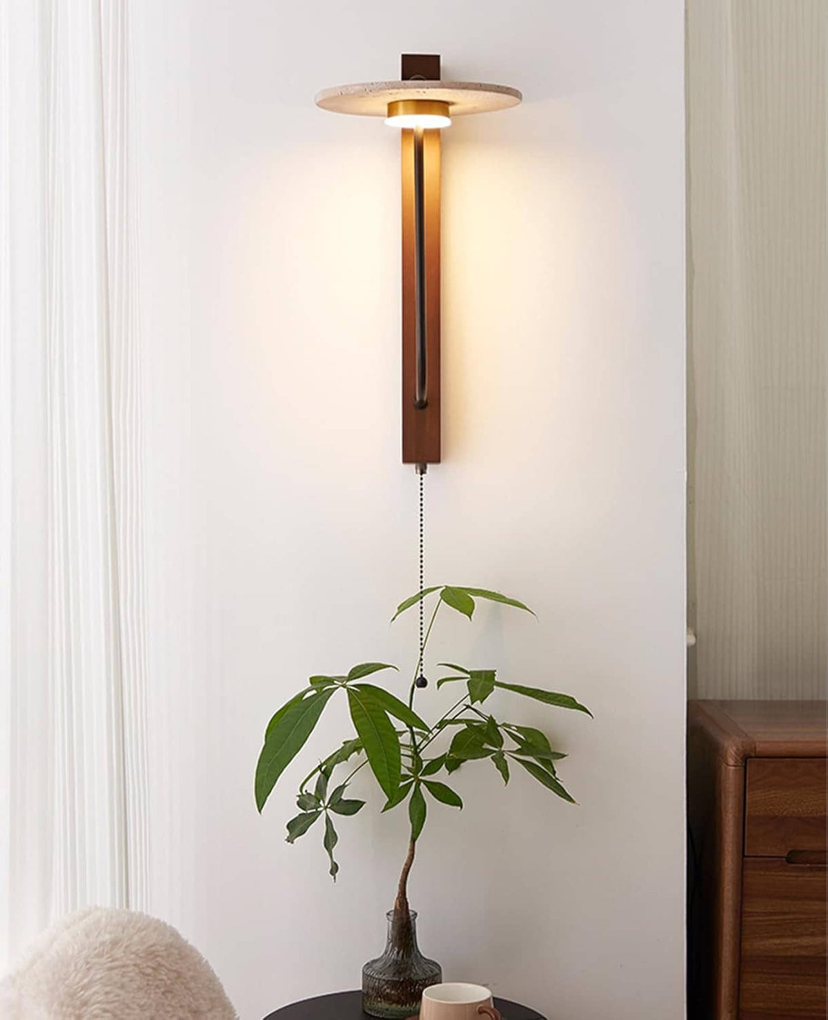 Wood and travertine wall sconce with black arm and pull cord, lit above a plant