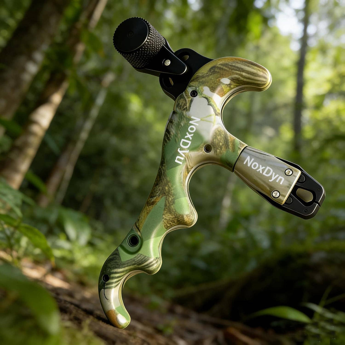 Archery bow thumb release hanging outdoors, black trigger with textured knob, green camo