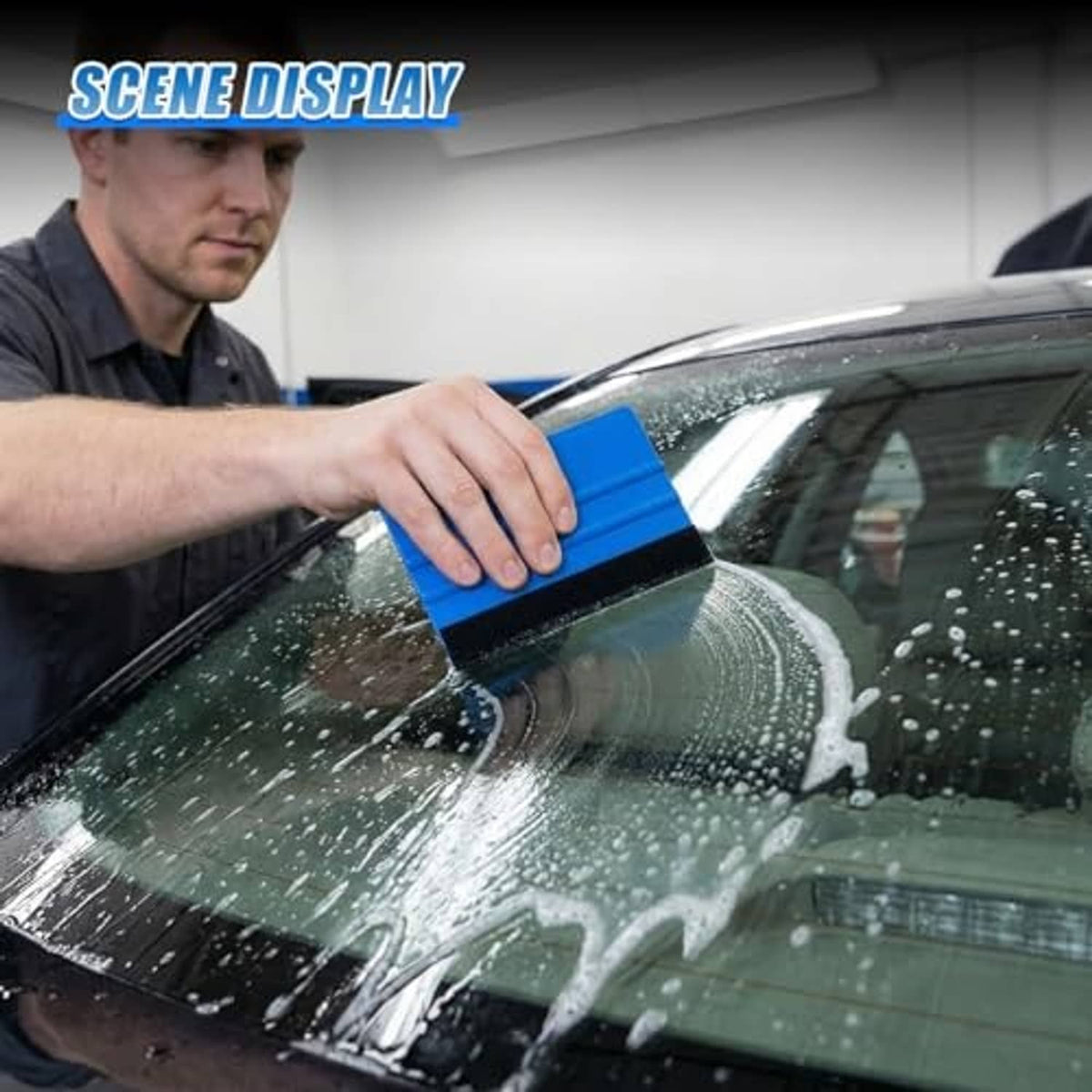 Blue felt-edge vinyl scraper squeegee held over car glass, black foam pad visible