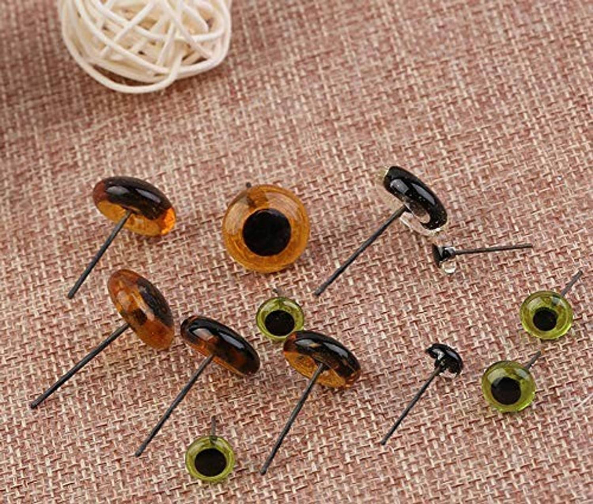 Amber and green glass eyes with needle prongs on textured fabric