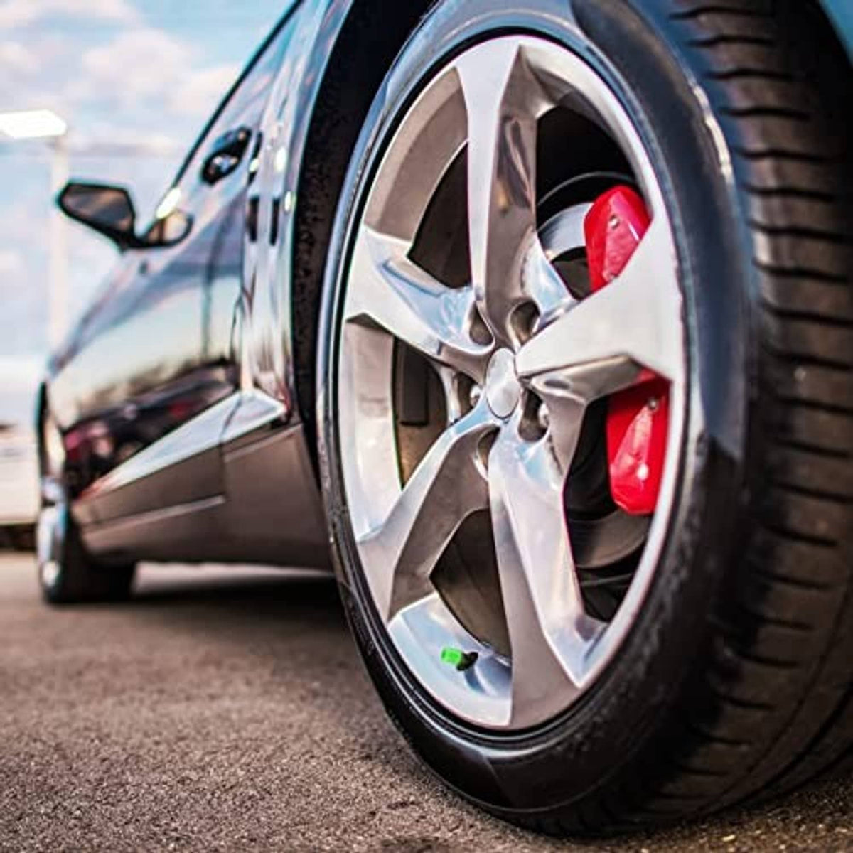Red glow-in-the-dark tire valve cap on a car wheel spoke near the tire