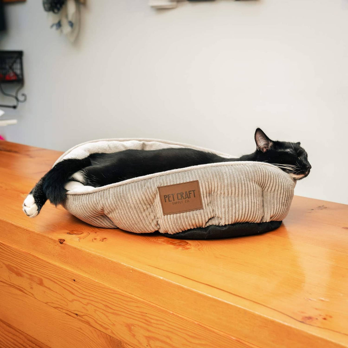 Beige and gray ribbed cat bed on floor; black cat curled up inside