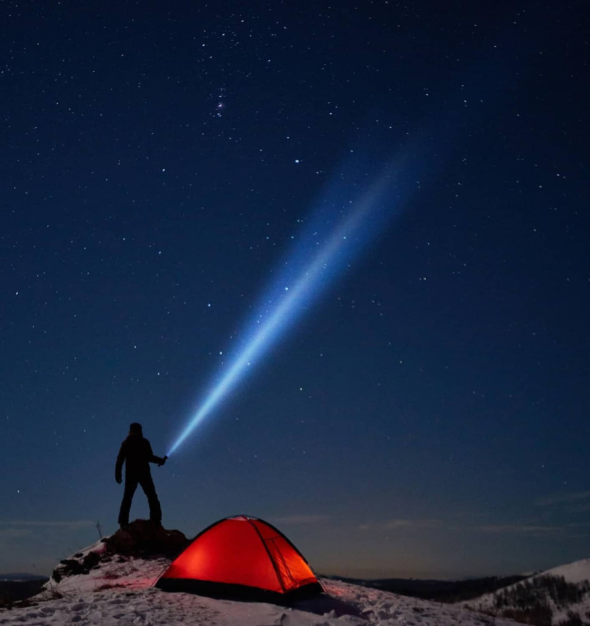 Flashlight beam illuminating a red camping tent on a snowy ridge at night