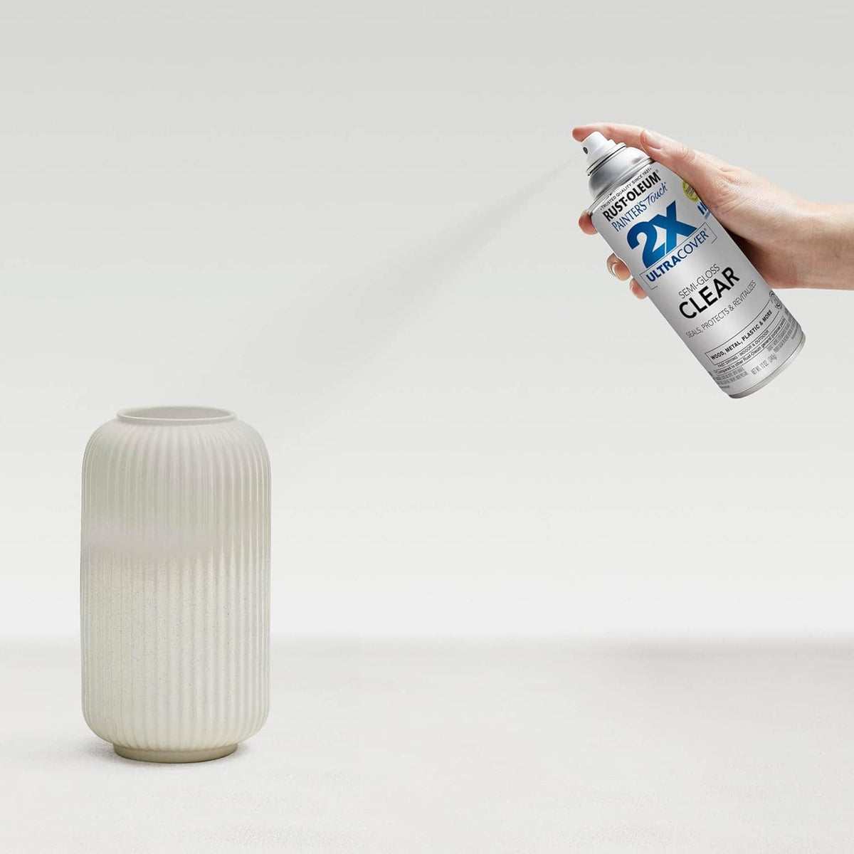 Hand holding semi-gloss clear spray paint can over a ribbed glass vase