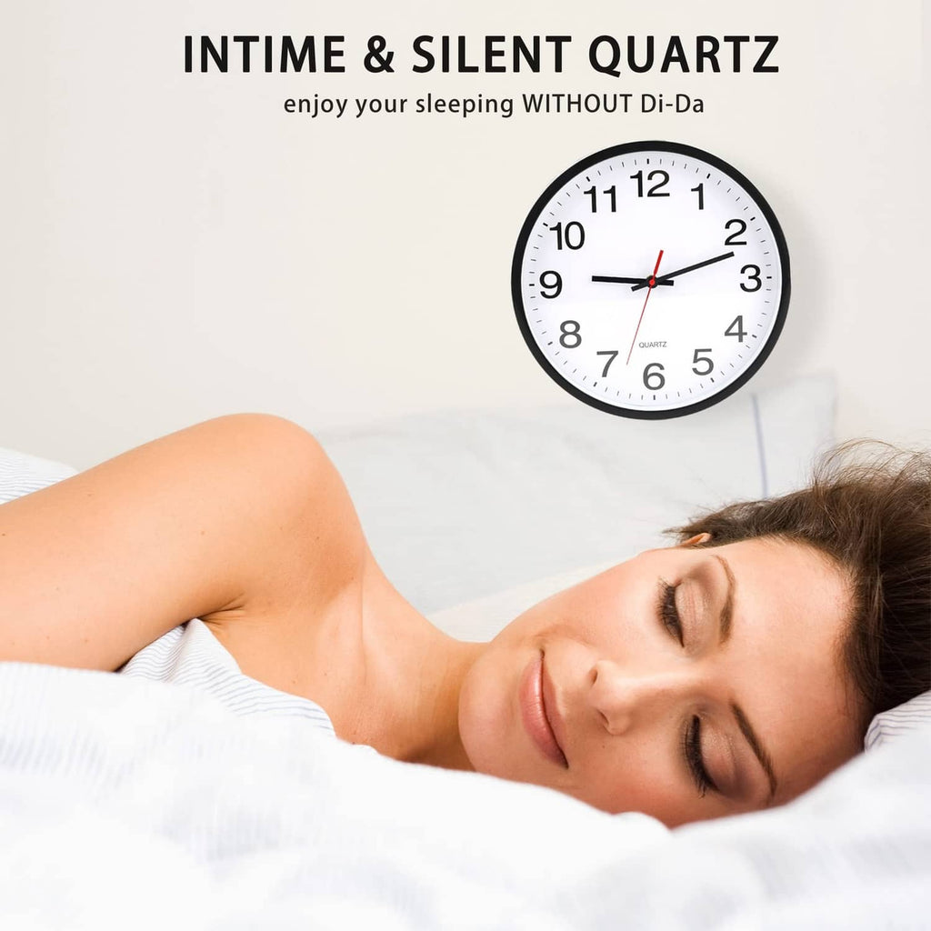 Black round wall clock with white dial and black numerals, red hands mounted above bedding.
