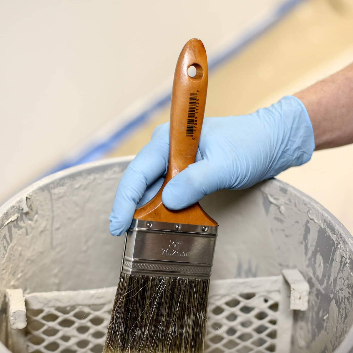 Blue nitrile glove hand holding paint brush over paint tray