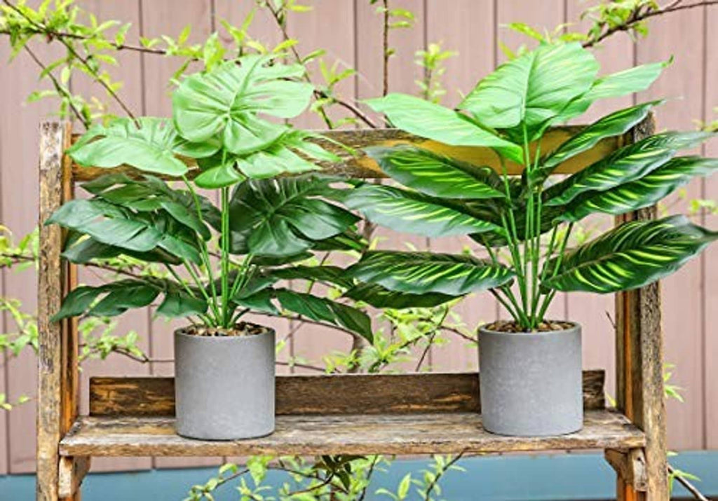 Two artificial potted tropical plants with glossy green leaves on gray pots