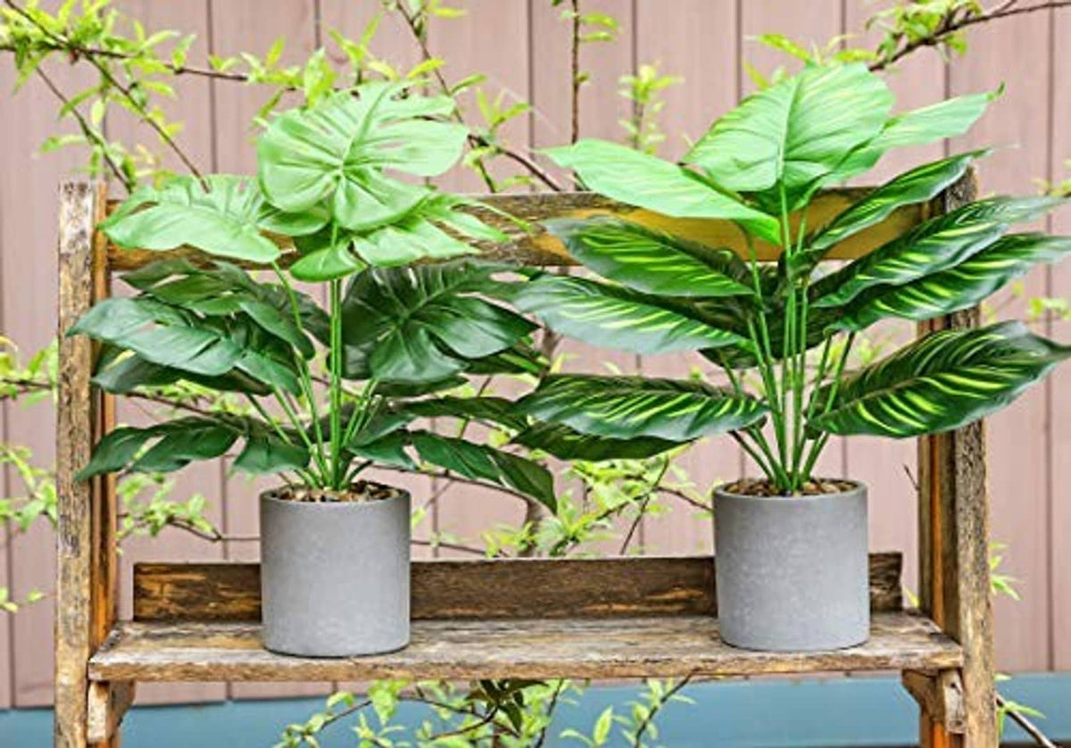 Two artificial potted tropical plants with glossy green leaves on gray pots