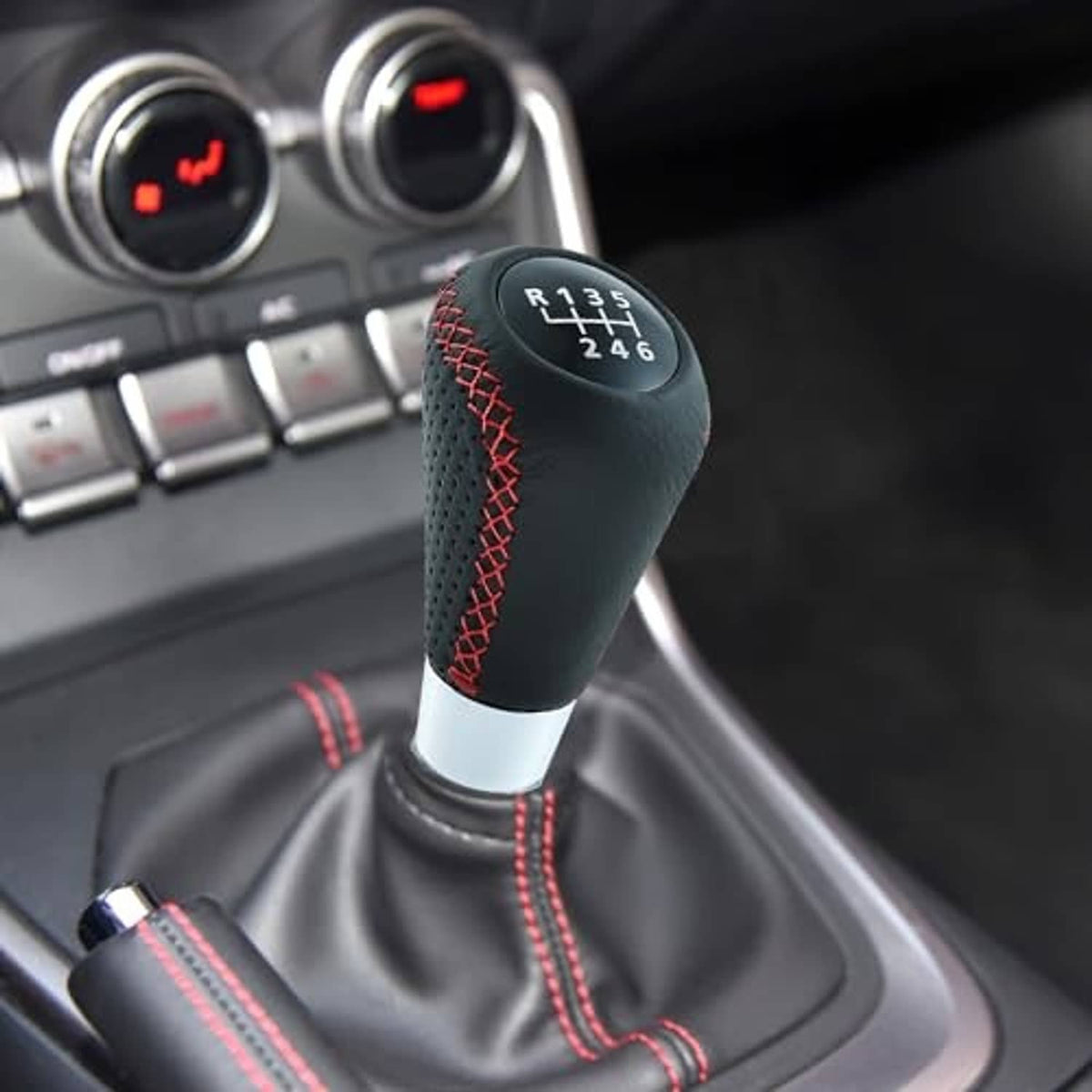 Manual shifter knob installed in car interior, black leather with red stitched grille and shift numbers