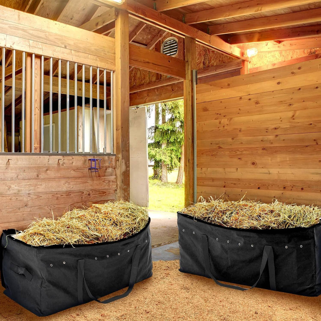 Two black hay storage bags with hay bedding inside and side handles in a barn stall