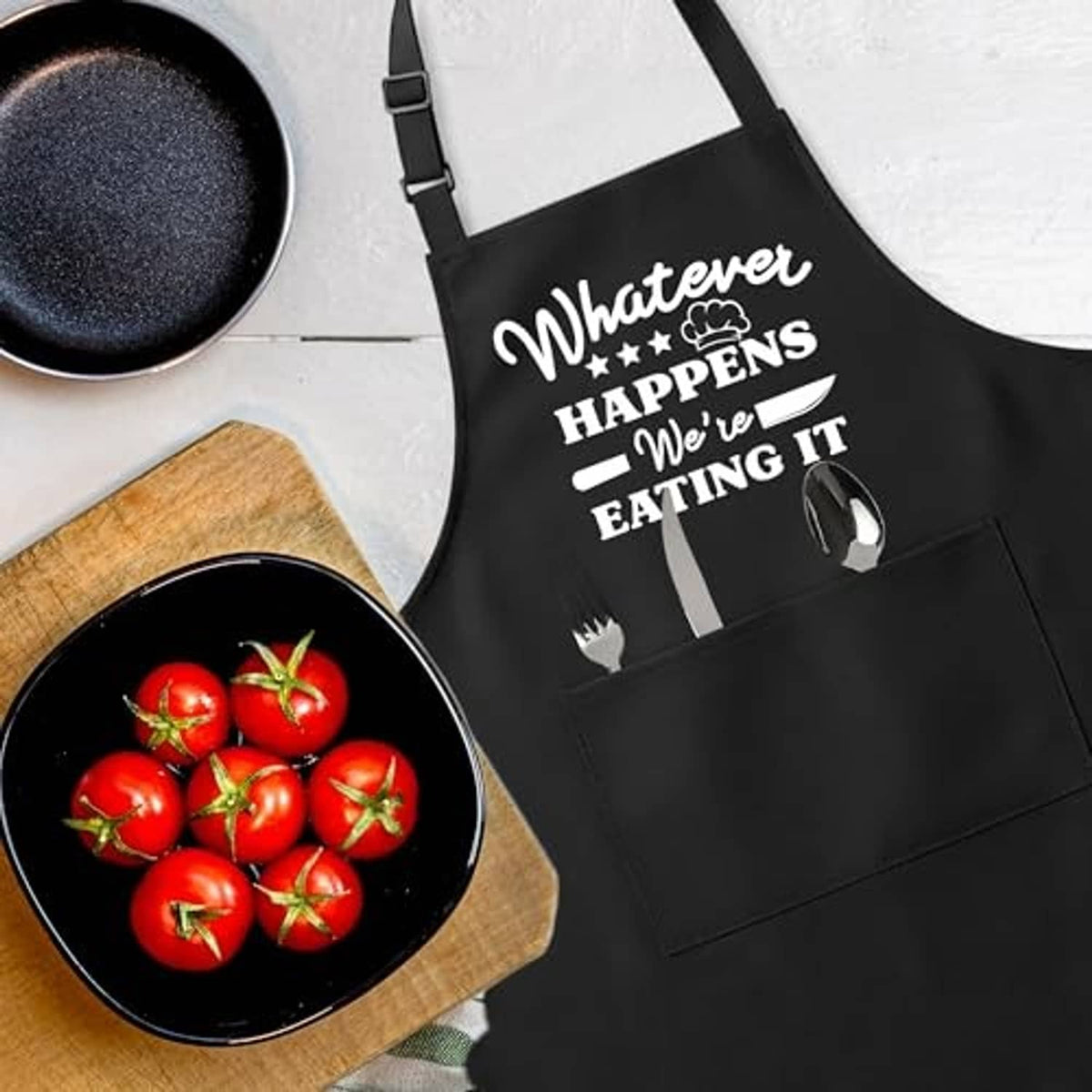 Black apron close-up with “Whatever happens we’re eating it” slogan and utensil icons