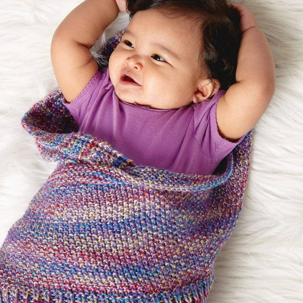Baby in purple outfit with multicolor knit blanket and buttoned edge