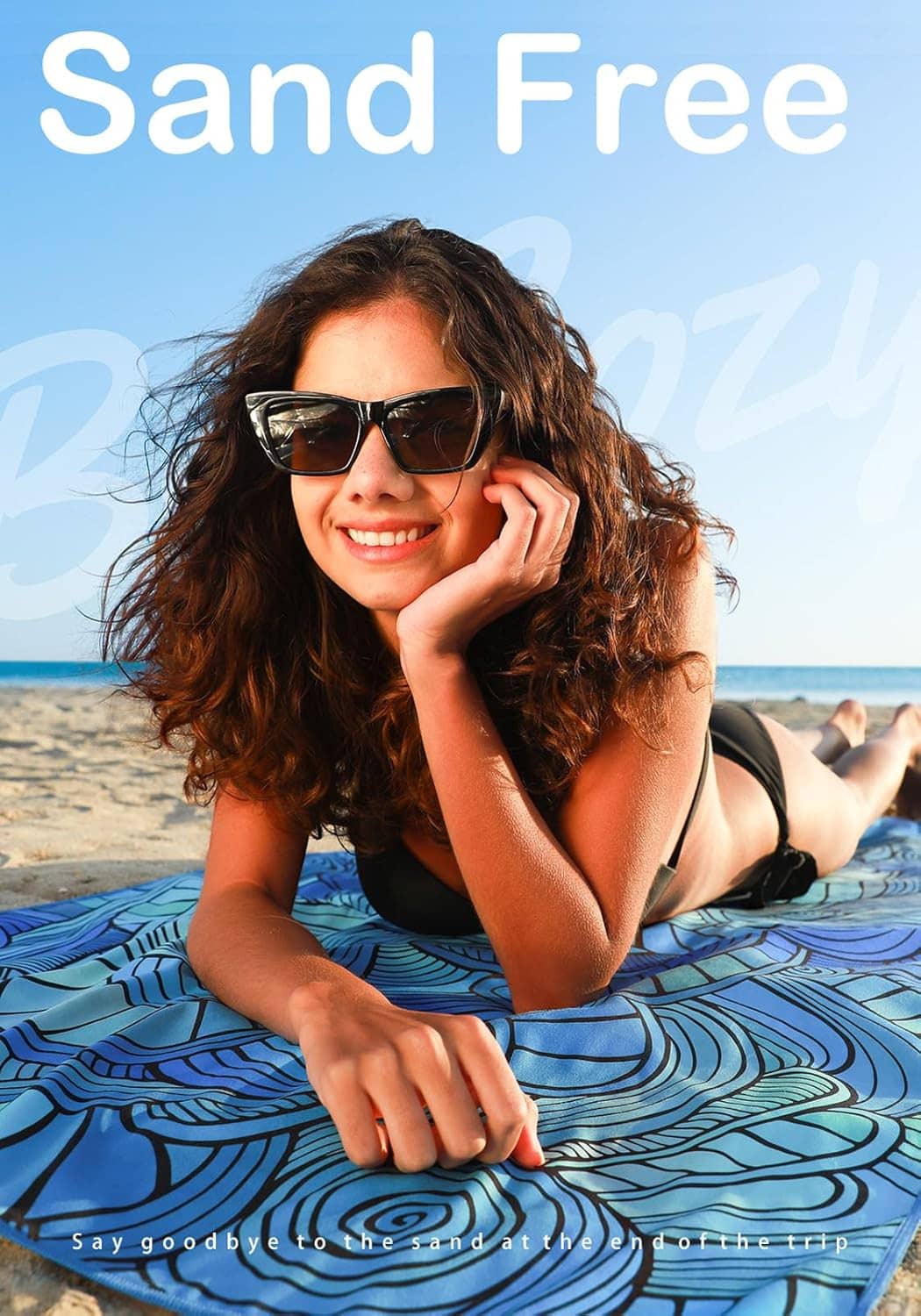 Blue swirl-pattern beach towel spread on sand under a sunny sky, held by a person
