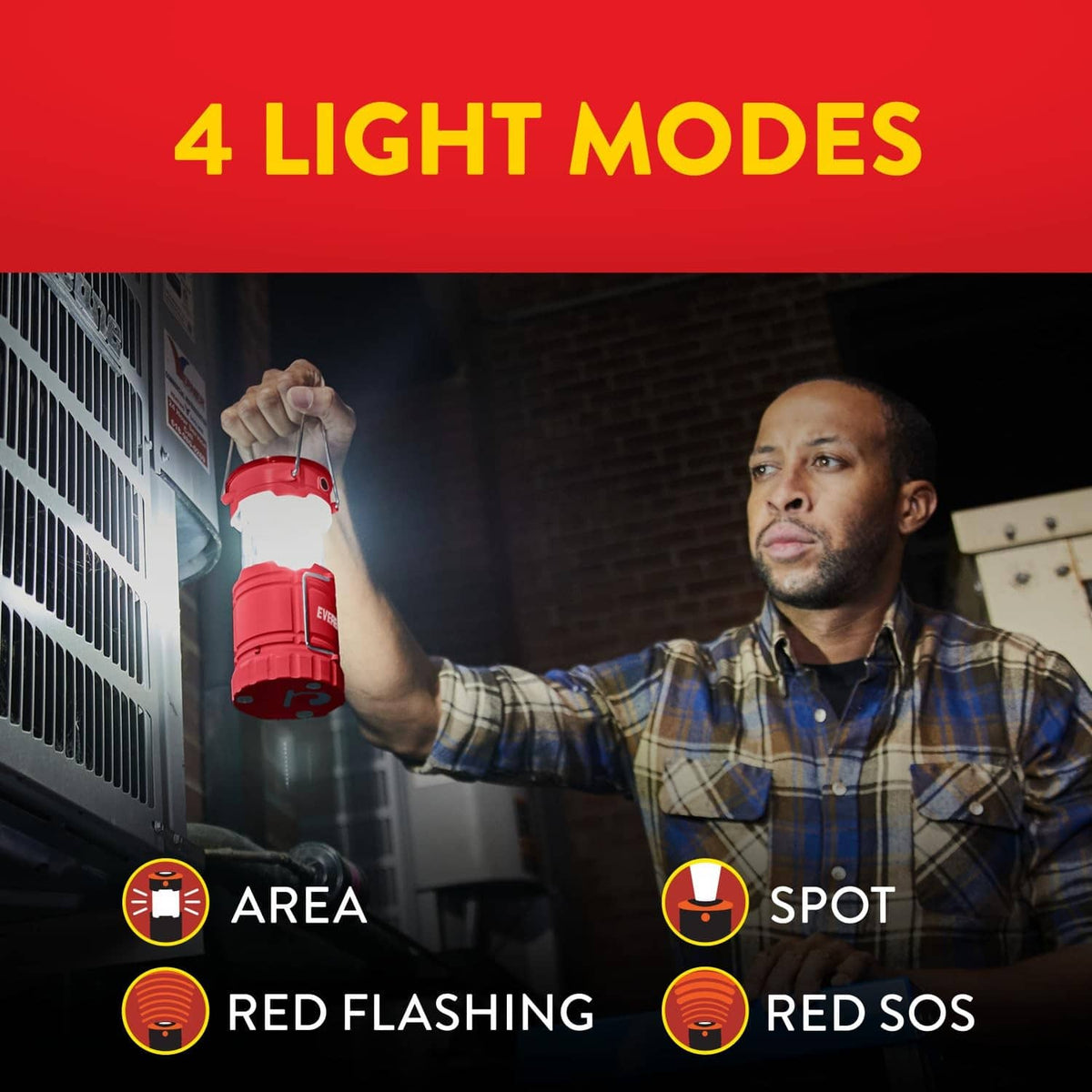 Red LED camping lantern held up by a person with folding metal carrying handles.