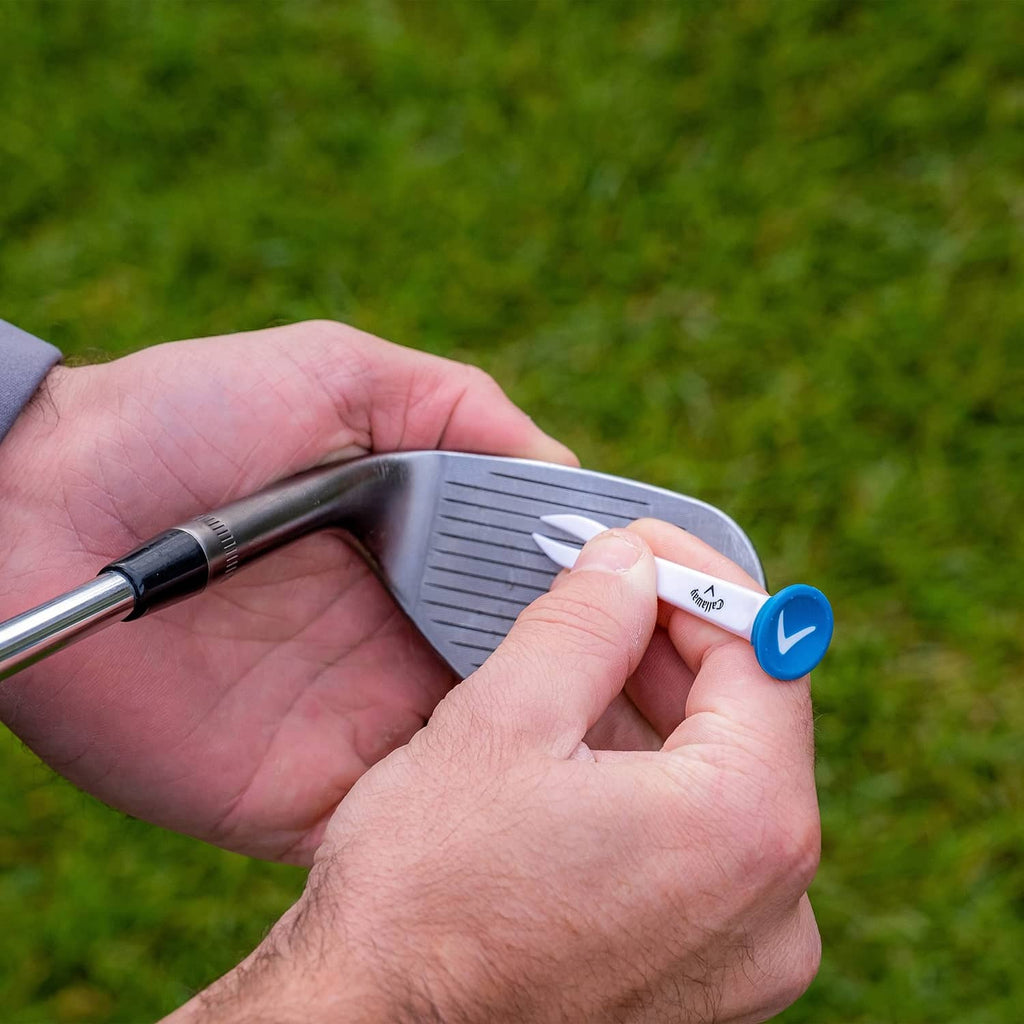 Hand placing a blue-tipped plastic golf tee into the grass