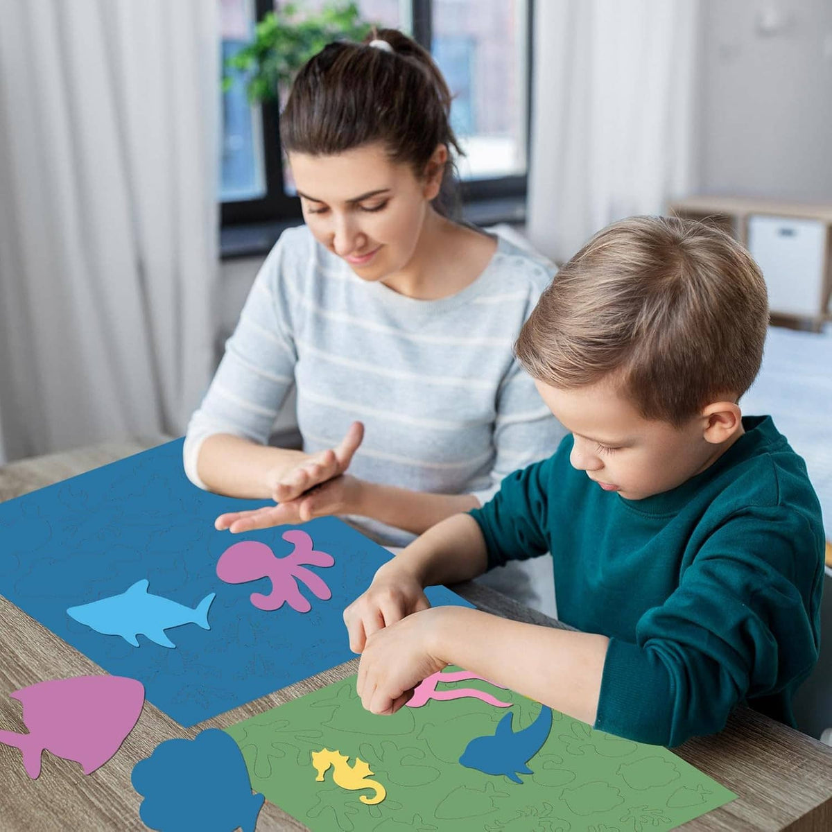 Child and adult arranging ocean animal cutout shapes on a large craft sheet