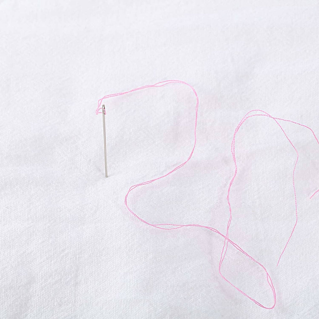 Pink thread with needle for hand sewing on white fabric