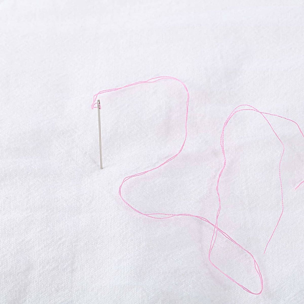 Pink thread with needle for hand sewing on white fabric