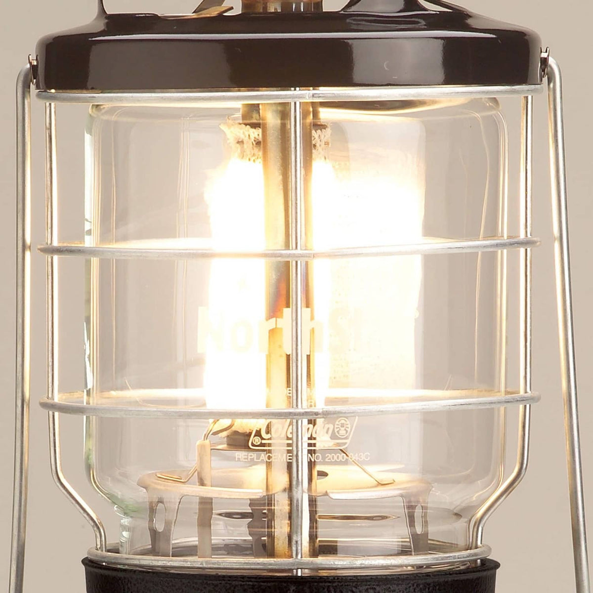 Coleman Northstar gas lantern with clear glass panels and glowing brass burner flame